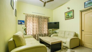 A living room with a sofa, a coffee table, a television, and a ceiling fan.