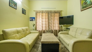 A living room with two beige sofas, a coffee table, a flat-screen TV, and floral curtains.