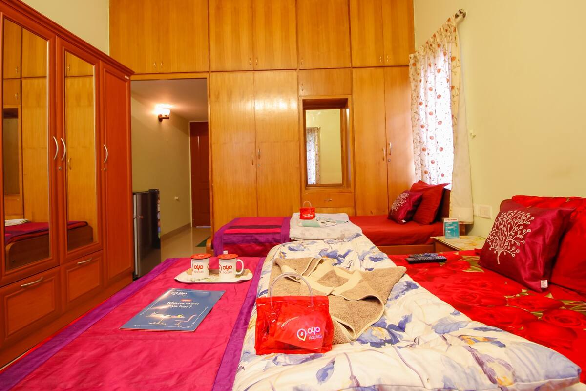 A hotel room with a bed, a wardrobe, a small table with a red bag, and a window with curtains.