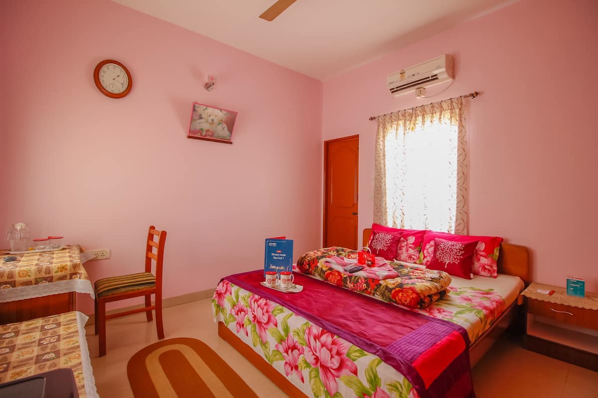 A pink-themed bedroom with a bed, a chair, a table, and a clock on the wall.