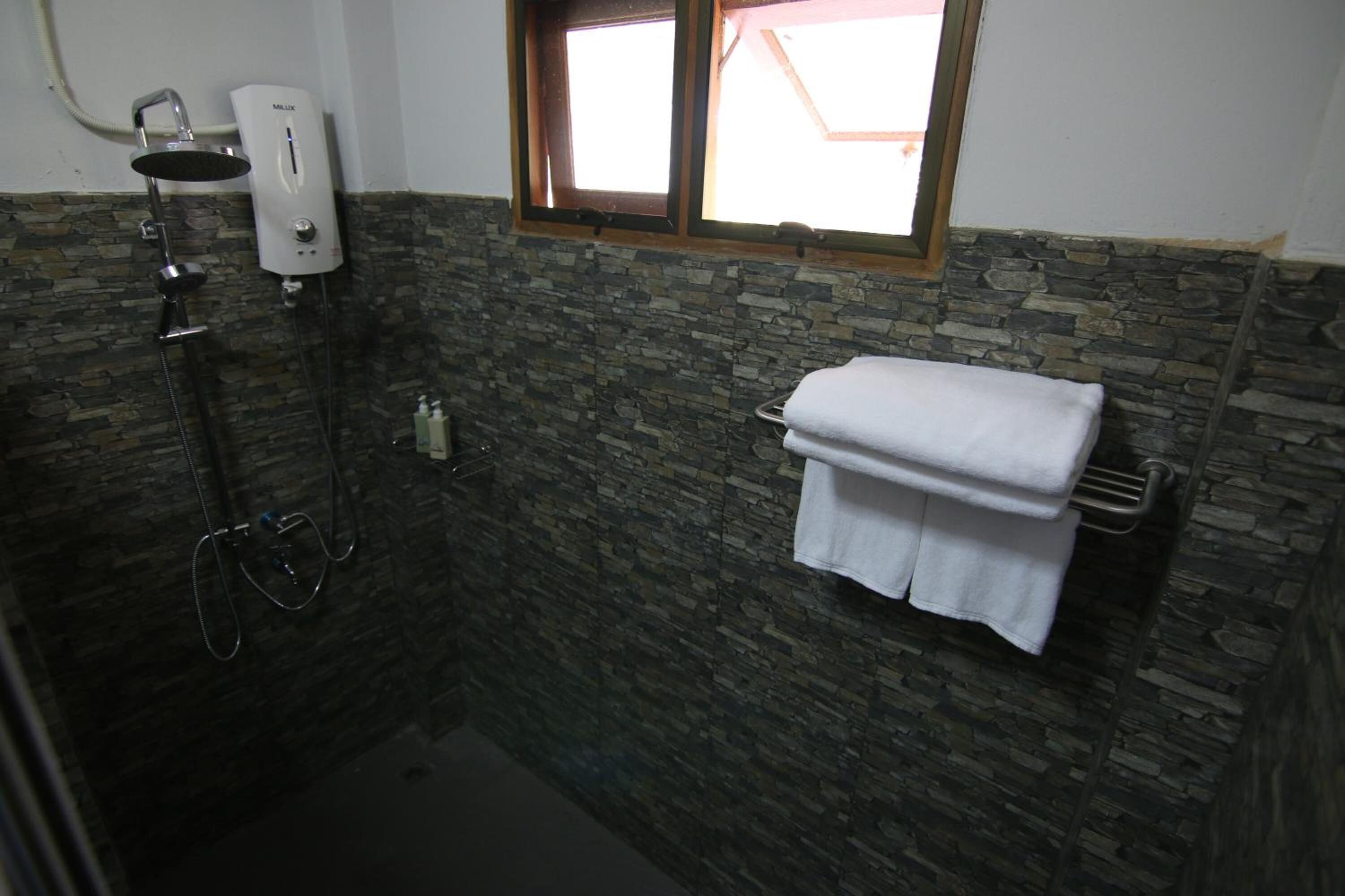 A bathroom with a stone wall, a window, a towel rack, and a handheld showerhead.