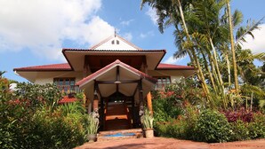 A traditional house with a central staircase, surrounded by lush greenery and palm trees. - Little Teak Home Stay (San Sai)