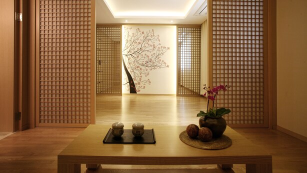 Ein traditioneller japanischer Raum mit Tatami-Boden, einem niedrigen Tisch mit Blumenvase und einer Wand mit Baumdekor.