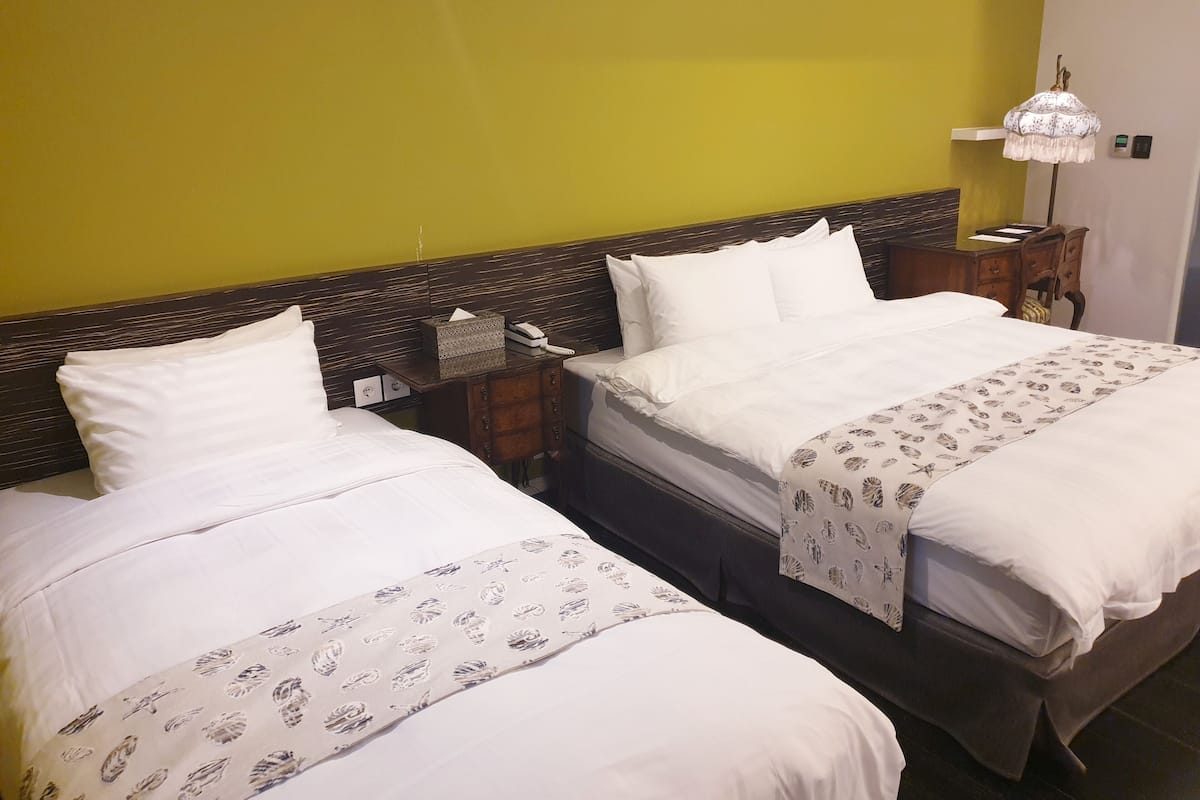 Une chambre d’hôtel avec deux lits, une table de chevet avec une lampe et un mur jaune.