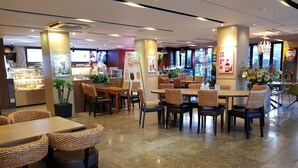 Ein modernes Restaurantambiente mit mehreren Tischen, Stühlen, einer Theke mit einer Auslage und Topfpflanzen.