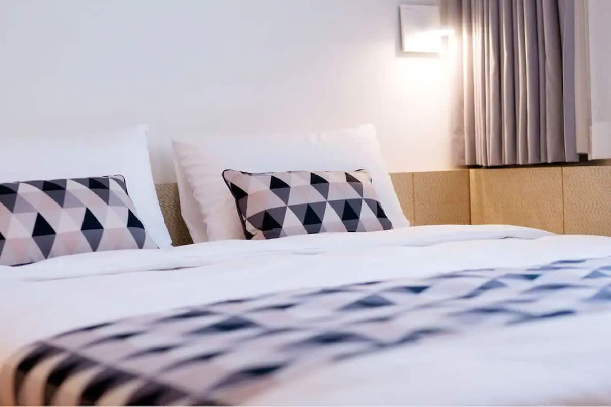 Une chambre d’hôtel avec un lit bien fait, deux oreillers aux motifs géométriques et une tête de lit dotée d’un luminaire.