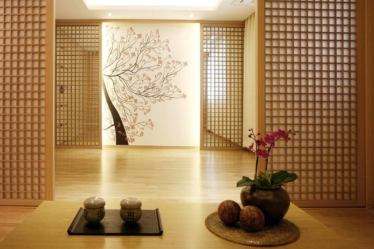Une pièce de style japonais traditionnel, avec un sol recouvert de tatamis, un paravent shoji, un mur décoré de calligraphies et une petite table sur laquelle sont posés un vase et deux tasses en céramique.