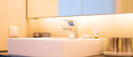 A bathroom with a white sink, a mirror, and a towel dispenser.