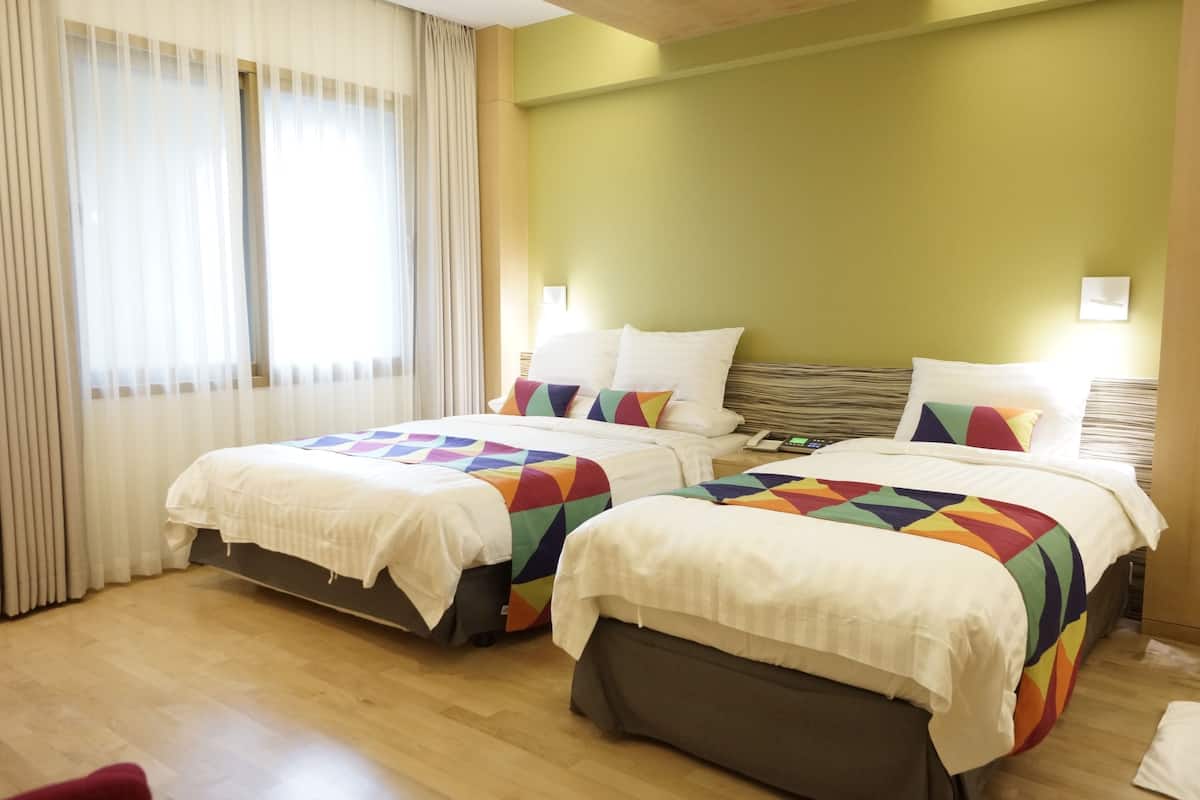 Une chambre d’hôtel avec deux lits, chacun agrémenté d’une couvre-lit aux motifs géométriques colorés, d’oreillers blancs et d’une tête de lit en bois.