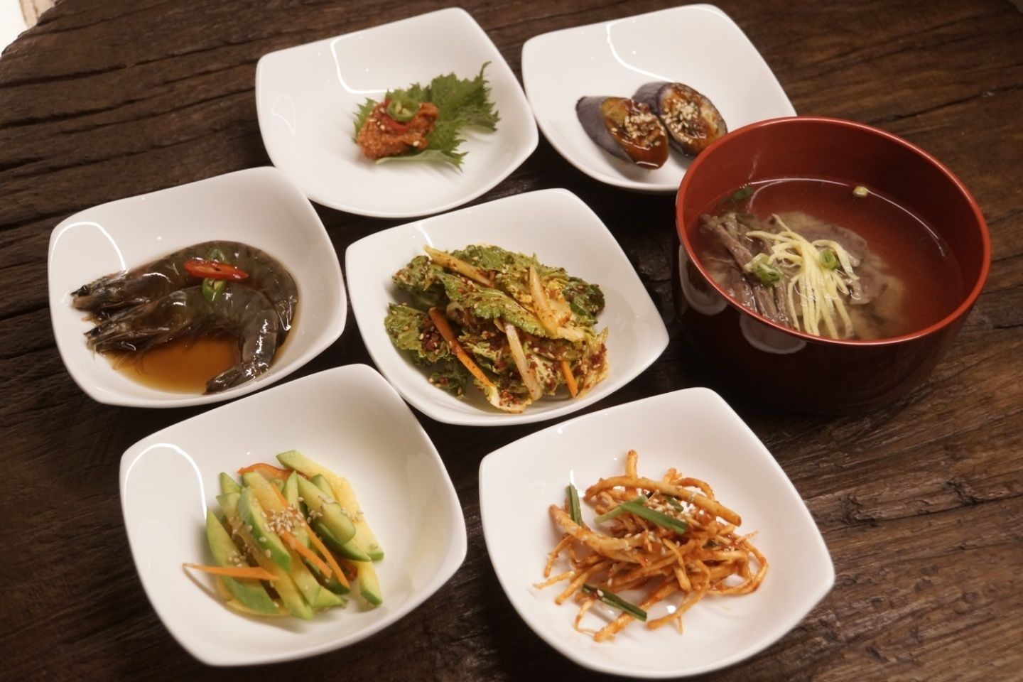 Una mesa con varios platos, incluyendo un tazón de sopa, una porción de fideos y varios pequeños recipientes con diferentes comidas.