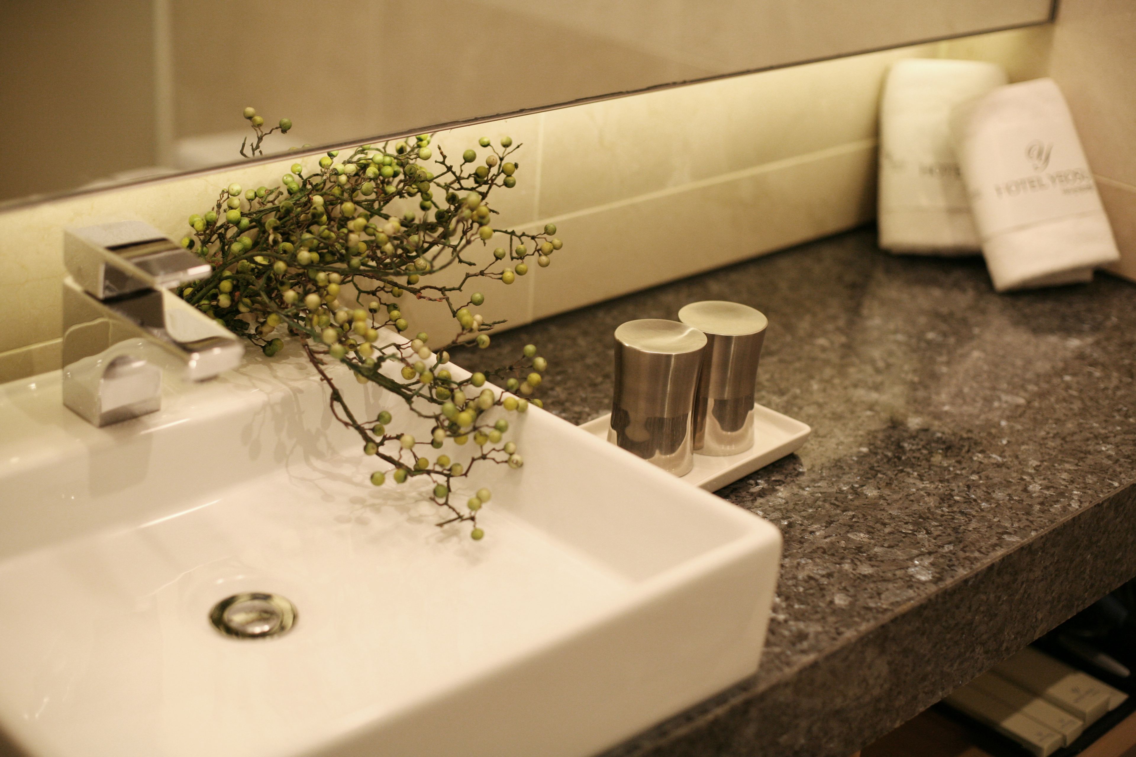 A bathroom sink with a mirror, a decorative branch, and toiletries on the countertop.