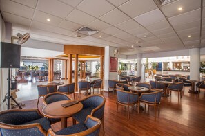 Un amplio comedor interior con varias mesas y sillas, suelo de madera e iluminación empotrada en el techo.