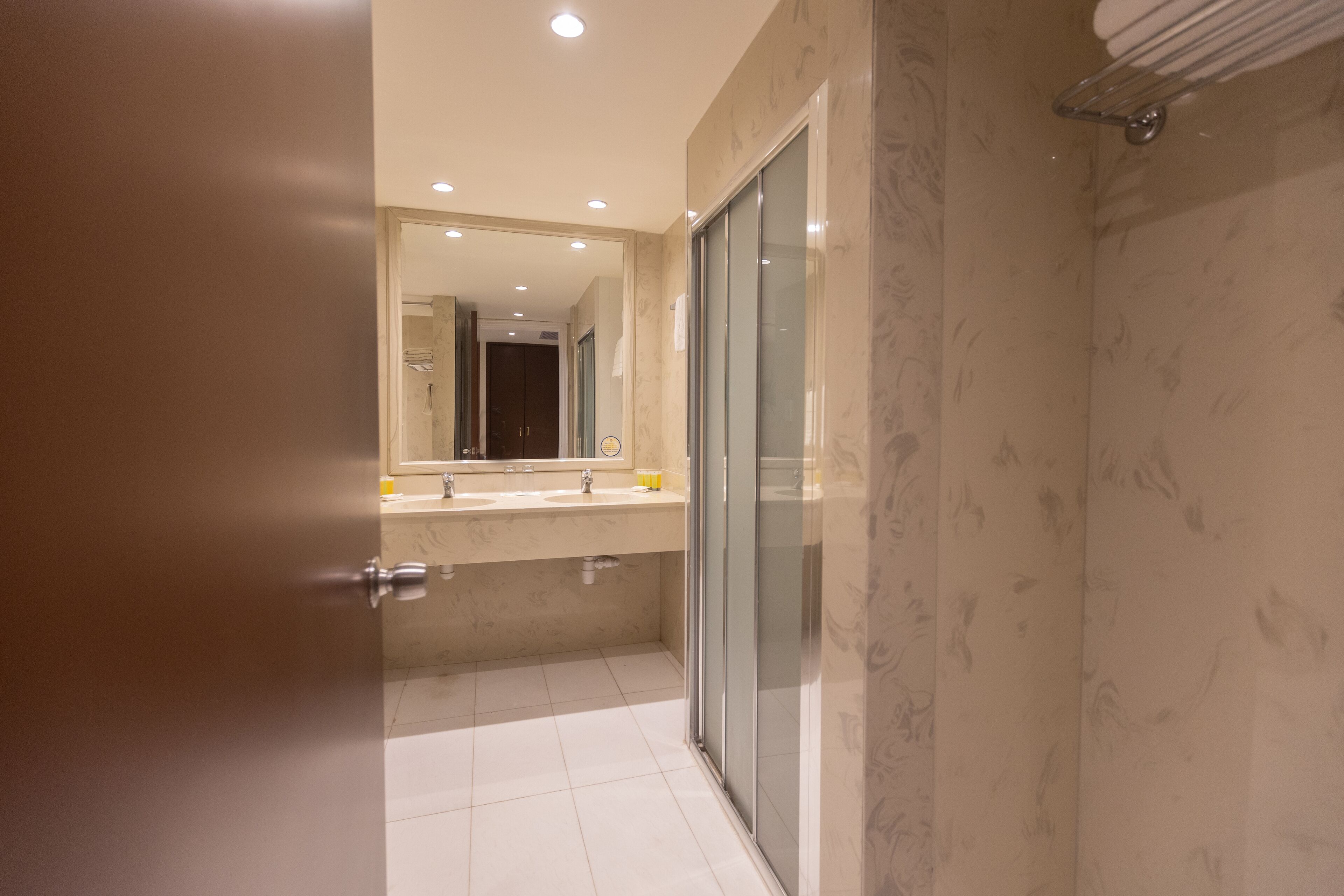 A modern bathroom with a glass shower enclosure, a large mirror, and a marble-tiled floor.