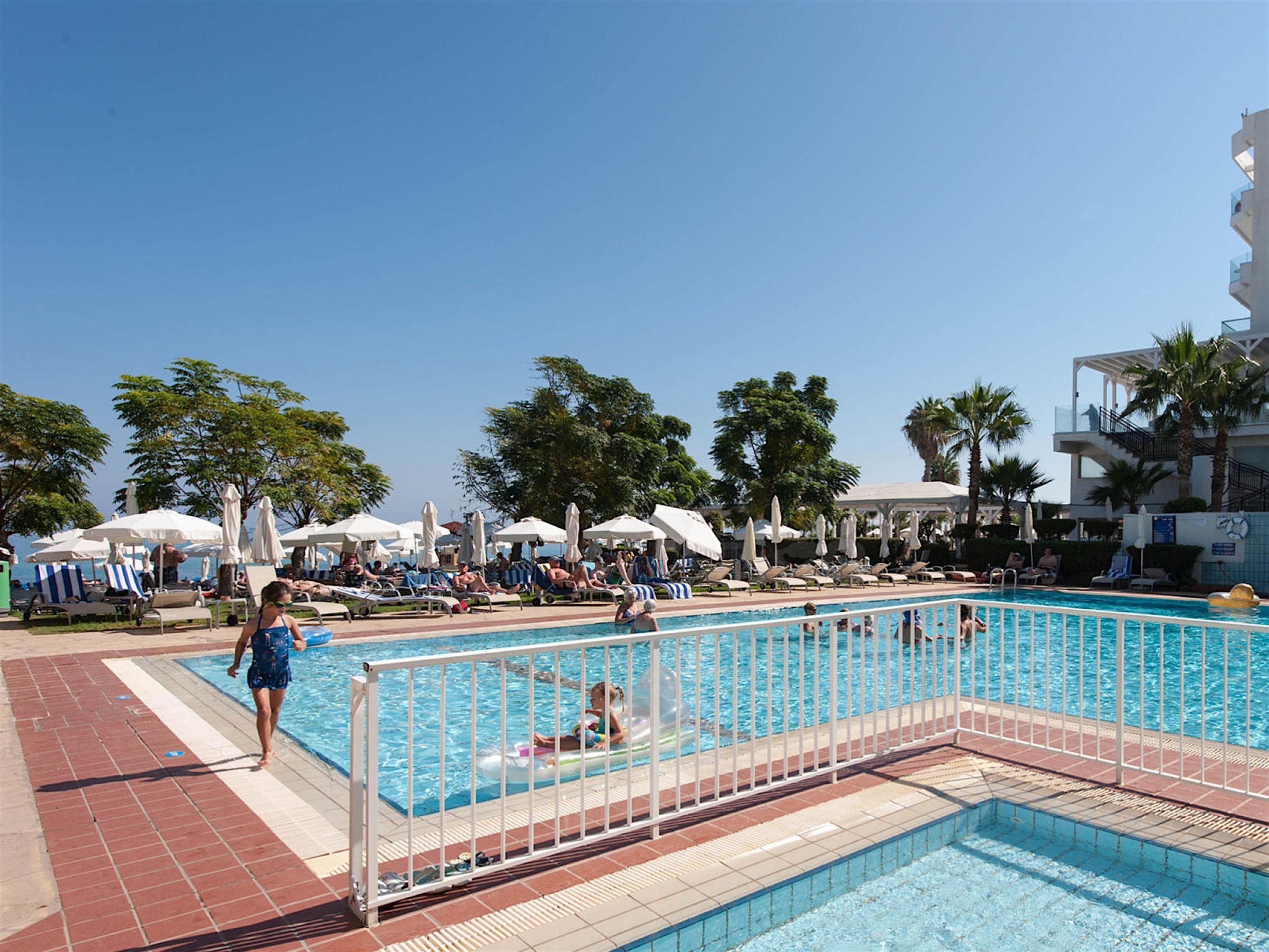 A pool area with multiple lounge chairs and umbrellas, surrounded by palm trees and a clear sky.