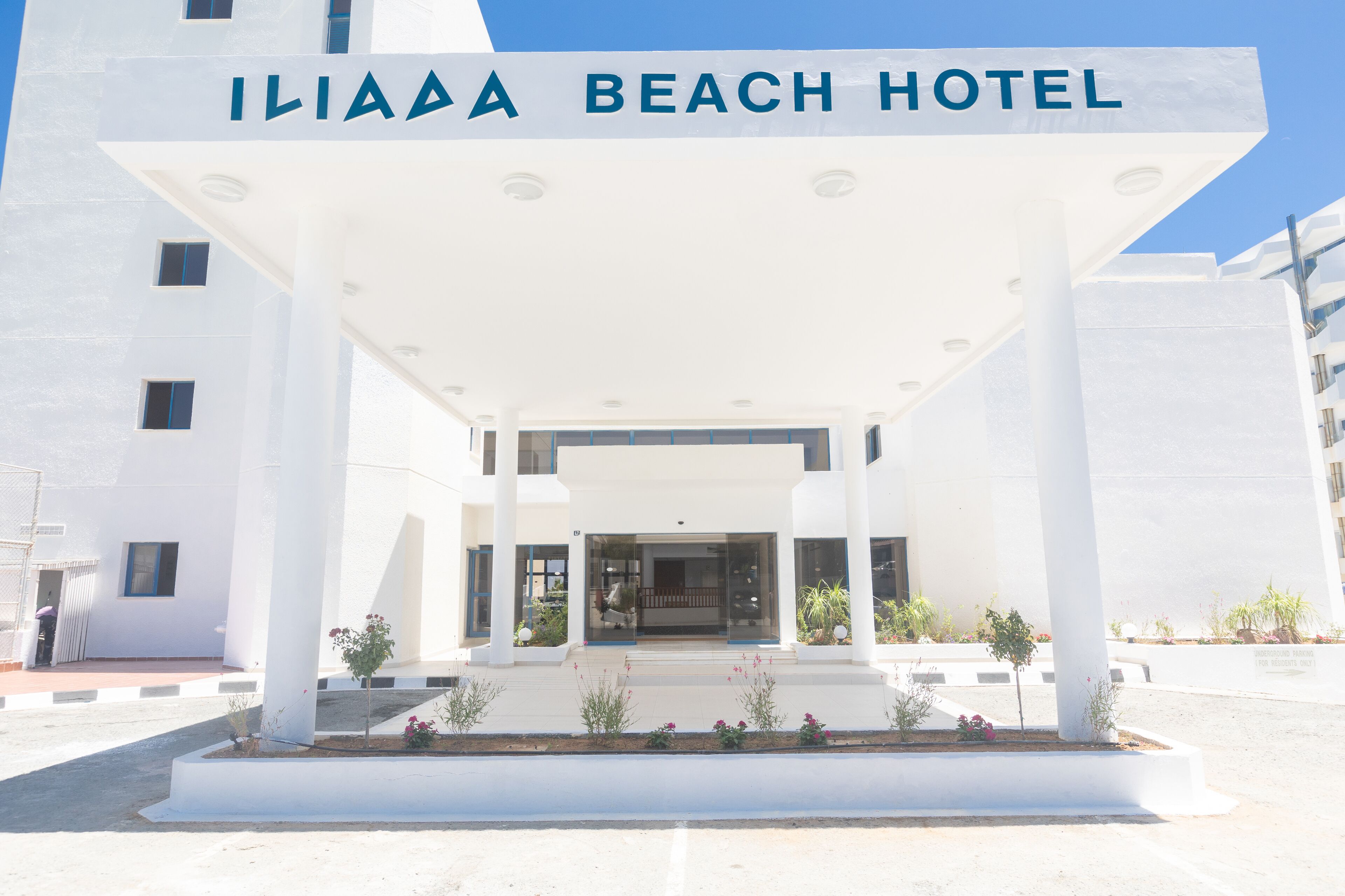 The entrance of the ILIAD BEACH HOTEL with a covered entrance, columns, and potted plants.