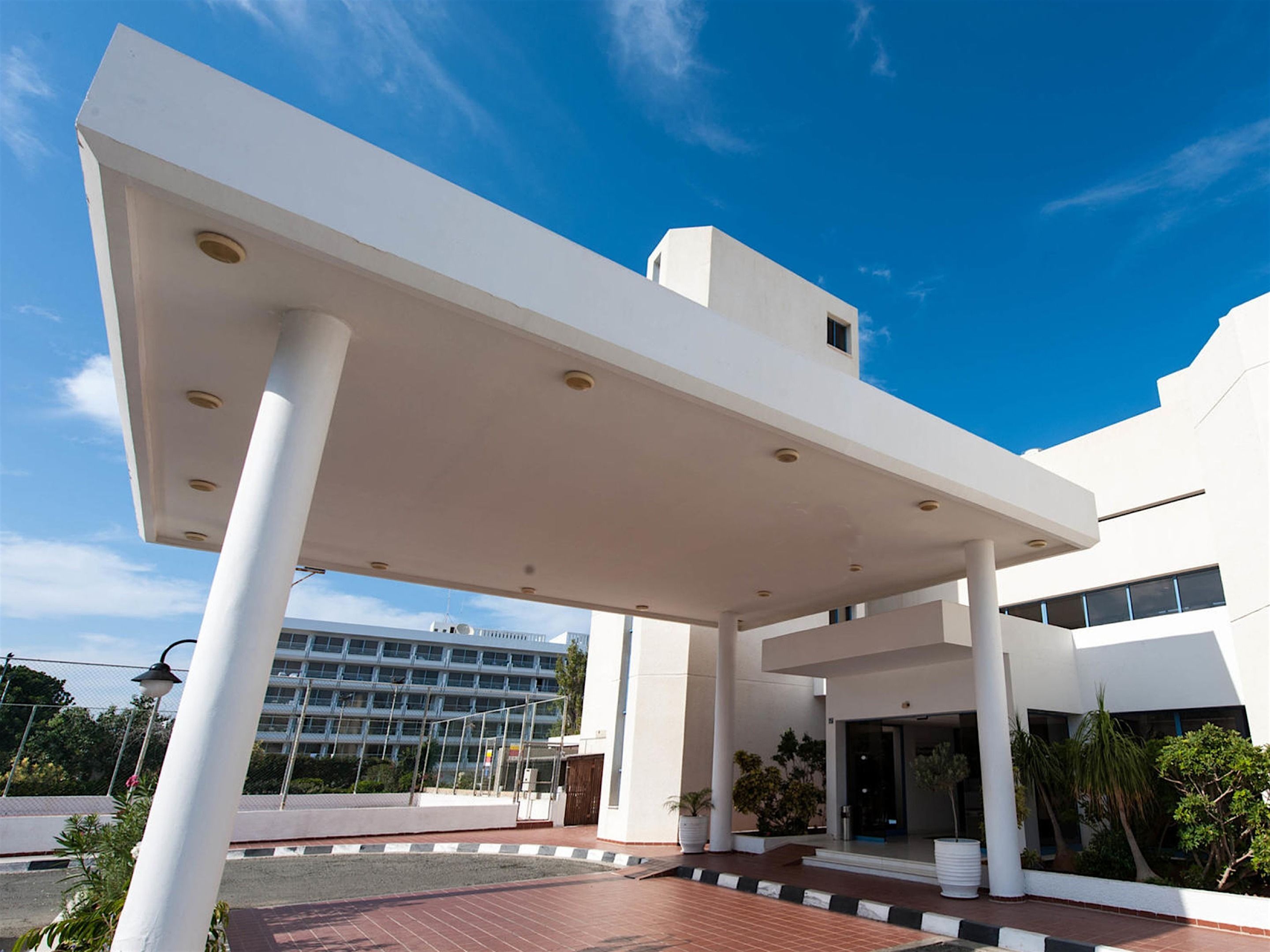 Un edificio moderno con entrada cubierta, grandes columnas y un cielo azul despejado.