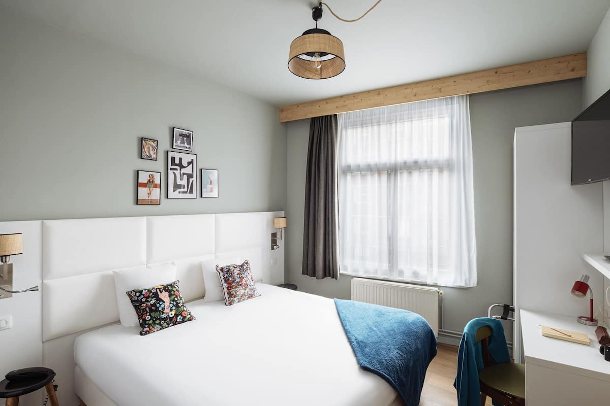 A bedroom with a bed, bedside table, lamp, and a window with curtains.