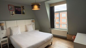 Una habitación de hotel moderna con una cama grande, lámparas de noche, una ventana con vistas a edificios y un aplique de techo.