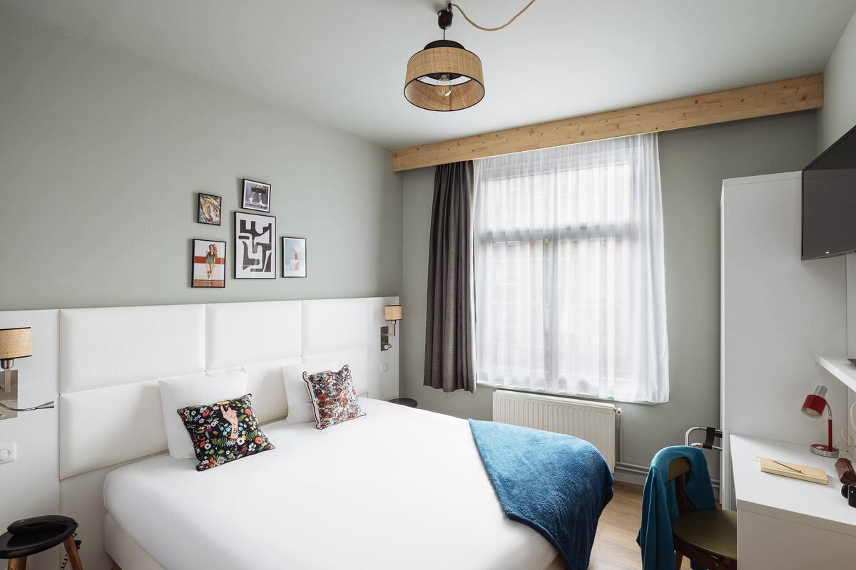 A bedroom with a bed, bedside table, lamp, and a window with curtains.