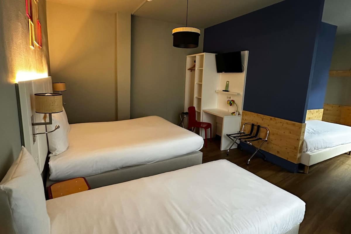 Habitación de hotel con dos camas, un escritorio, una silla, un televisor y una lámpara.