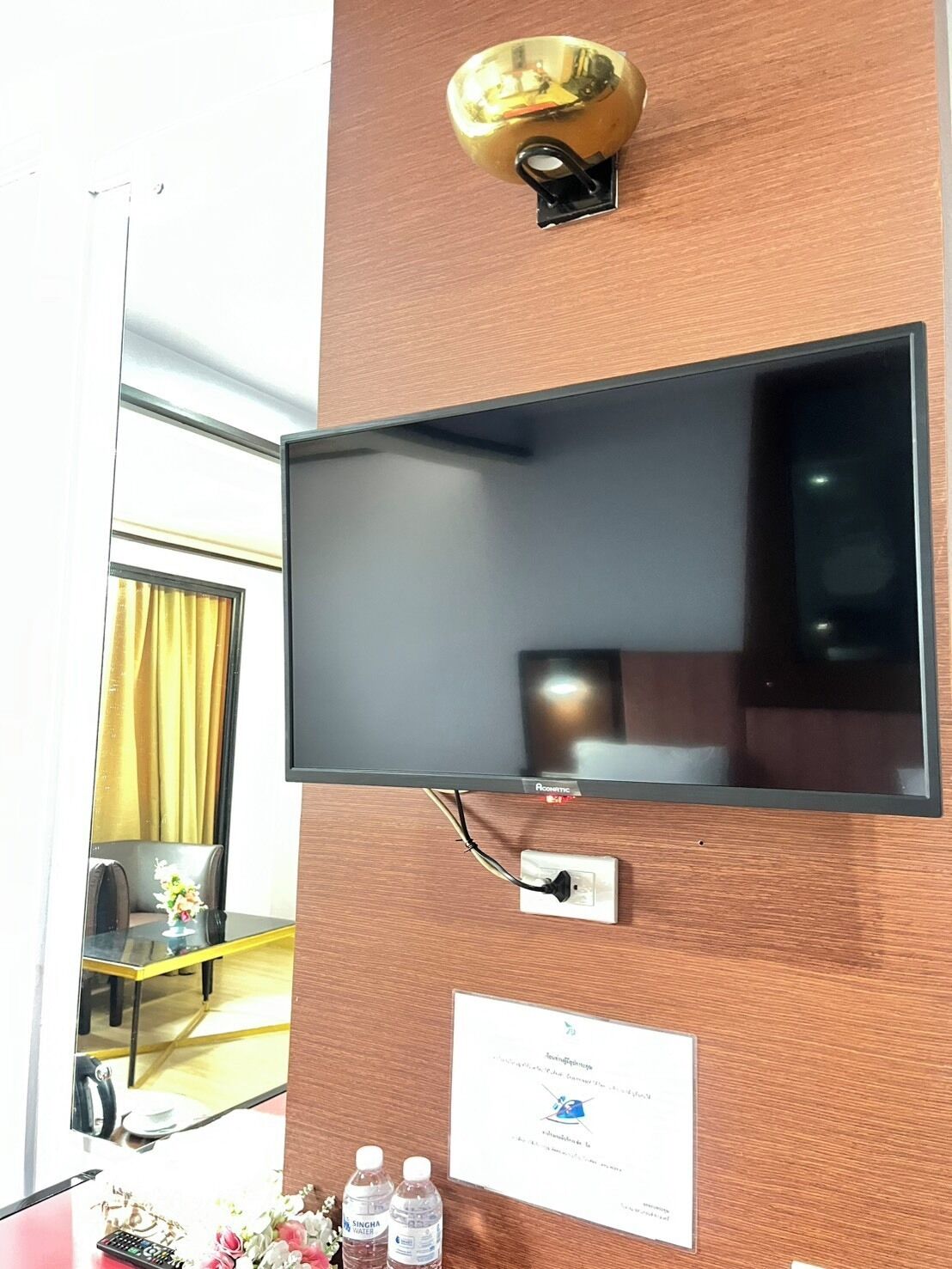 A flat-screen TV mounted on a wooden wall, a wall socket, and a small sign with text.