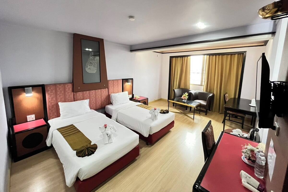 A hotel room with two beds, a desk, a chair, a TV, and a window with curtains.