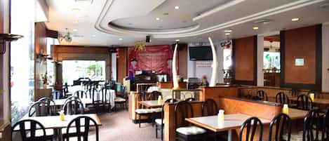 Un restaurante con cabinas y mesas, una barra y una pantalla de televisión.