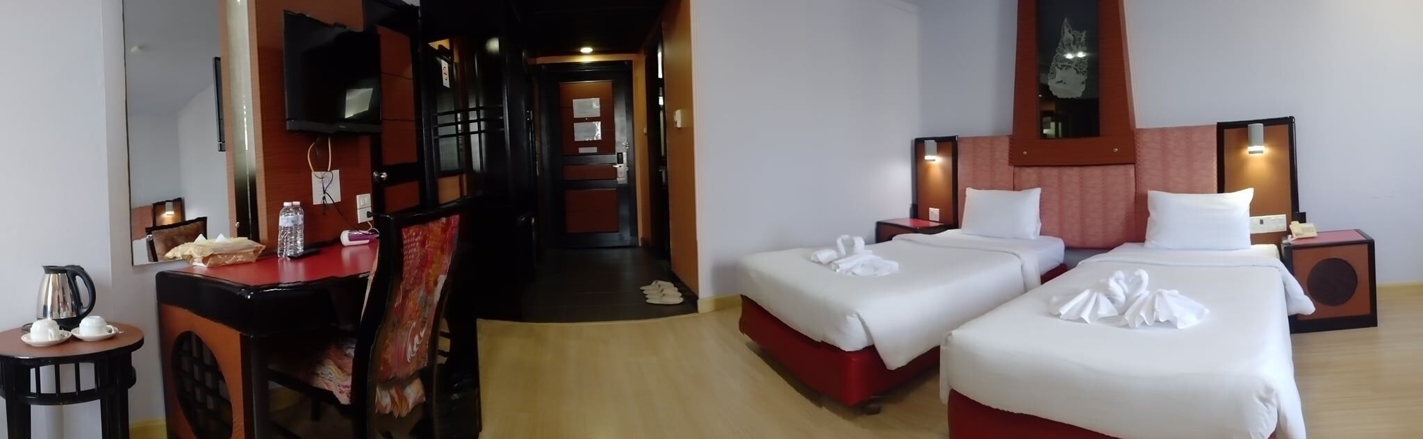 A hotel room with two beds, a desk with a chair, a mirror, and a small table with a kettle and cups.