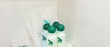 A bathroom with white tiles, a black countertop, and a tray holding four bottles of shampoo and a packet of soap.