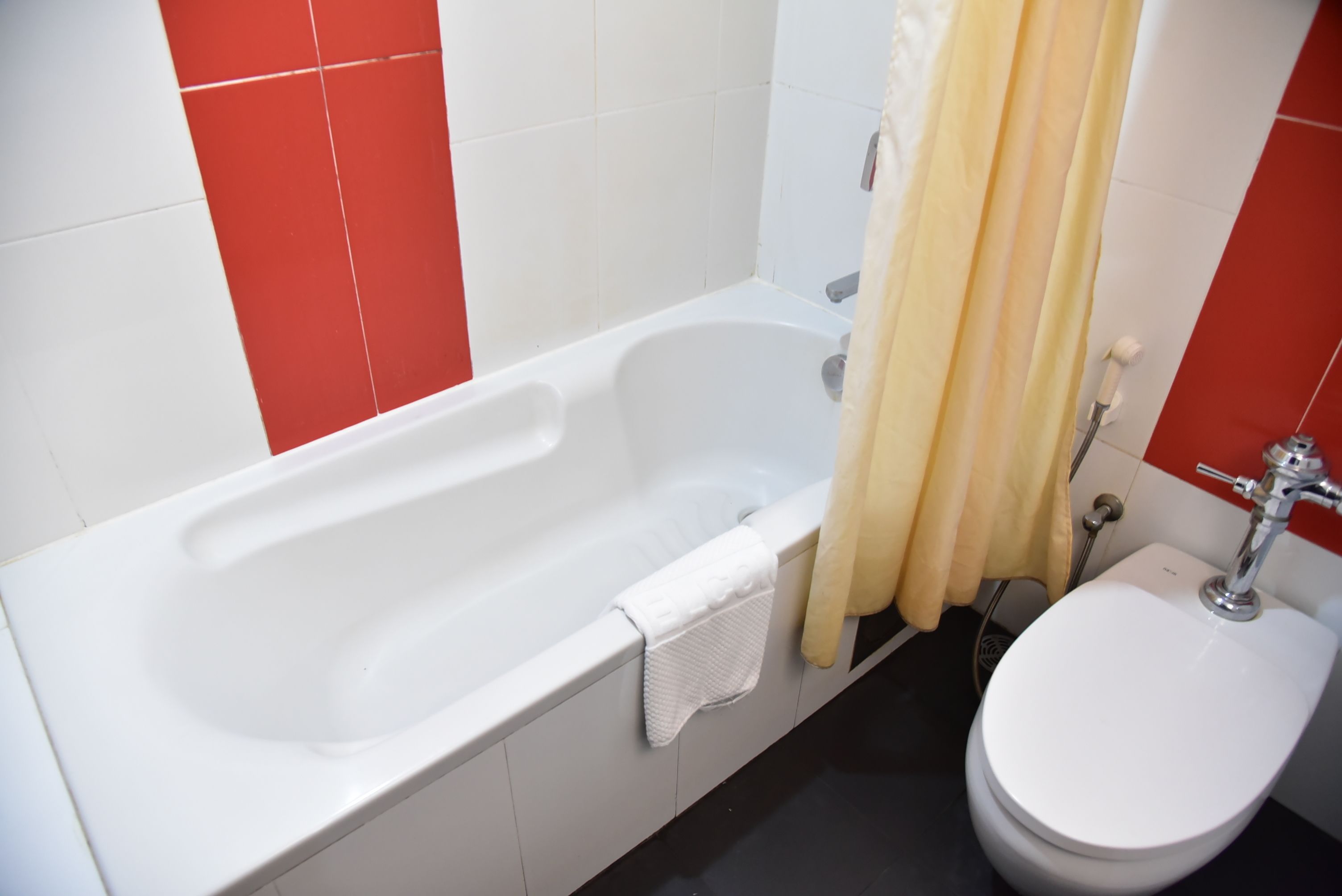 A bathroom with a white bathtub, a white toilet, and red and white tiled walls.