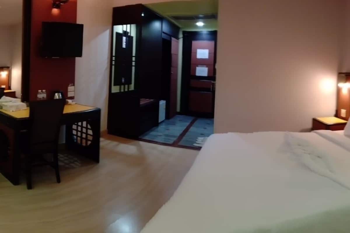 A hotel room with a bed, bedside tables, a desk with a chair, a television, and a door leading to a hallway.