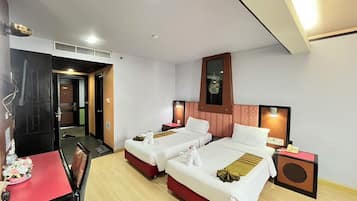 A hotel room with two beds, a desk, and a chair. There is a mirror above the beds and a small table with a red tablecloth.