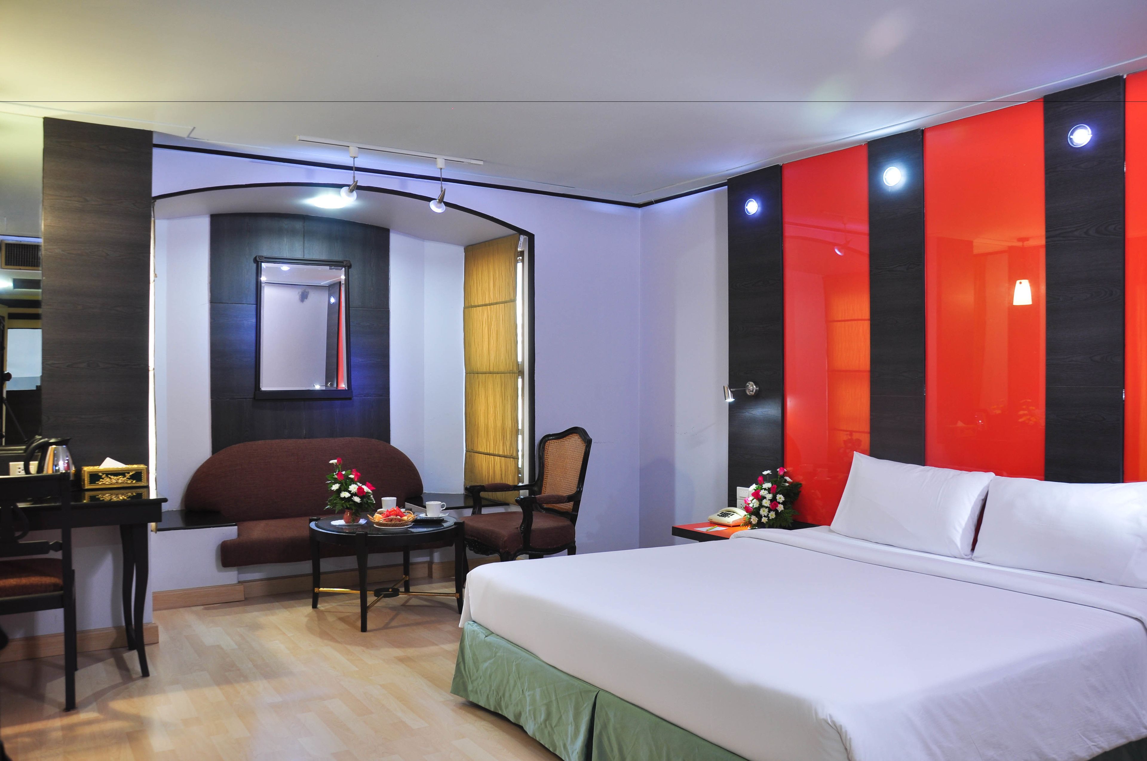 Habitación de hotel con cama, escritorio, silla y una mesita con un jarrón de flores.