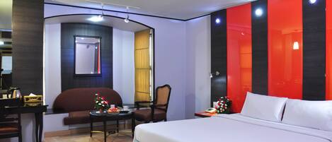 Habitación de hotel con cama, escritorio, silla y una mesita con un jarrón de flores.