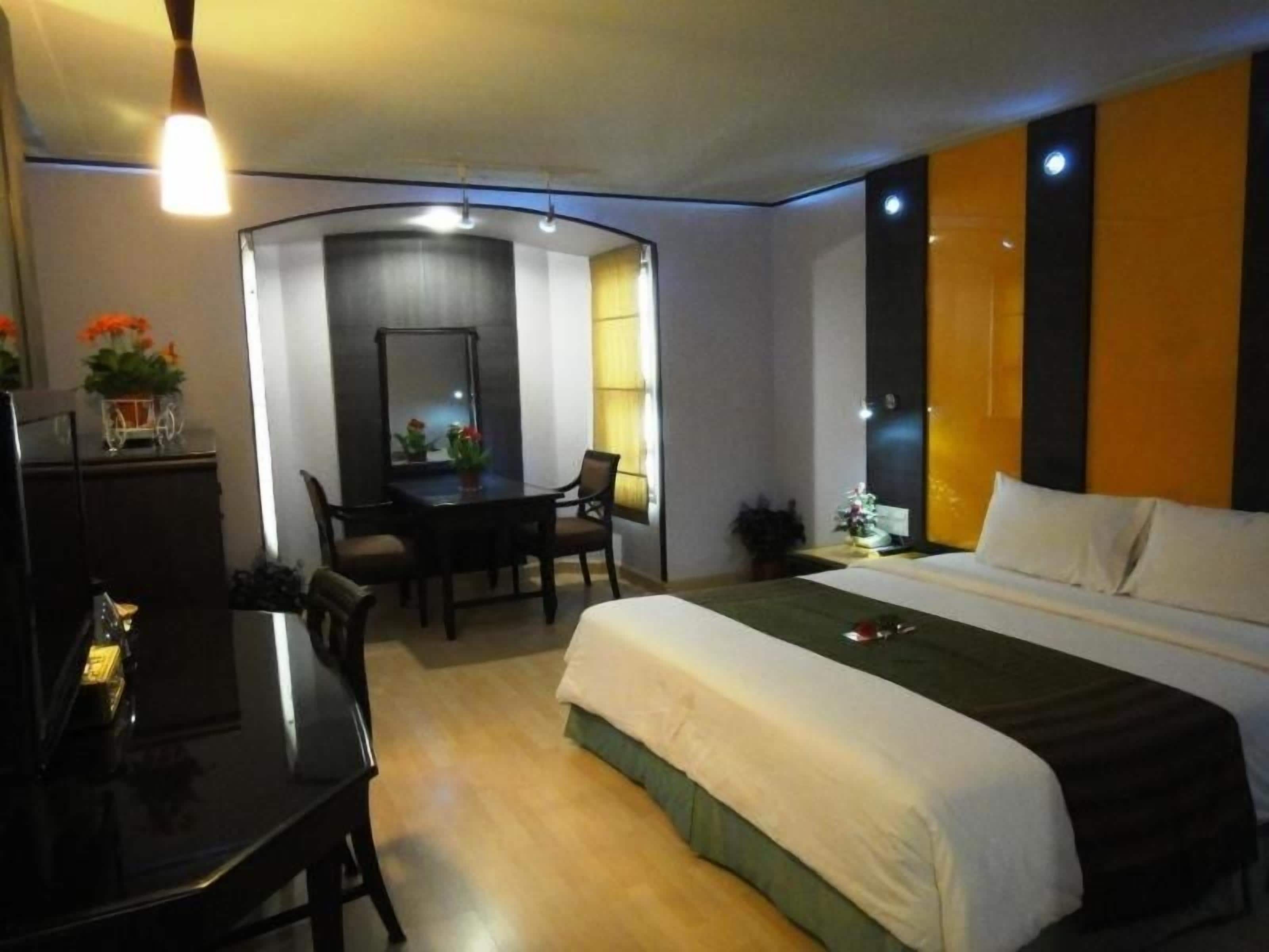 A hotel room with a bed, a desk, a chair, a mirror, and a small table with a plant.