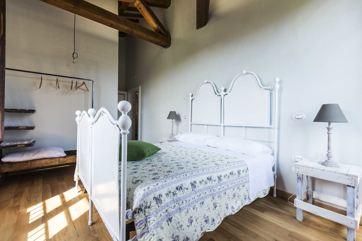 Ein Schlafzimmer mit einem weißen Bett, Holzboden und einem kleinen Nachttisch mit einer Lampe.