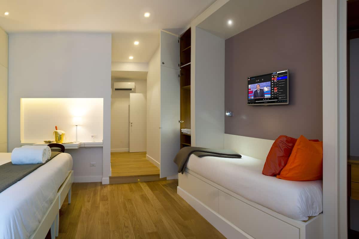 Ein Hotelzimmer mit zwei Betten, einem Fernseher, einem Schreibtisch und einem begehbaren Kleiderschrank.