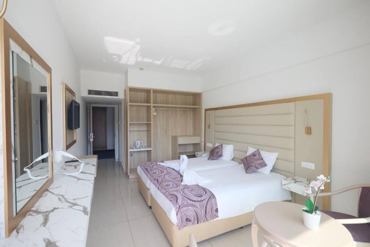 A modern hotel room with a large bed, a walk-in closet, a seating area with a table, and a mirror.