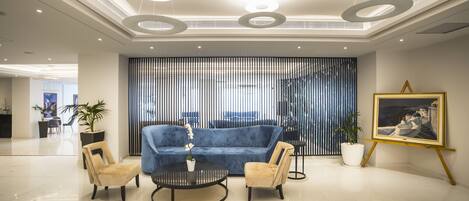 Un vestíbulo moderno con un sofá azul, dos sillones, una mesita de café y un cuadro en la pared.