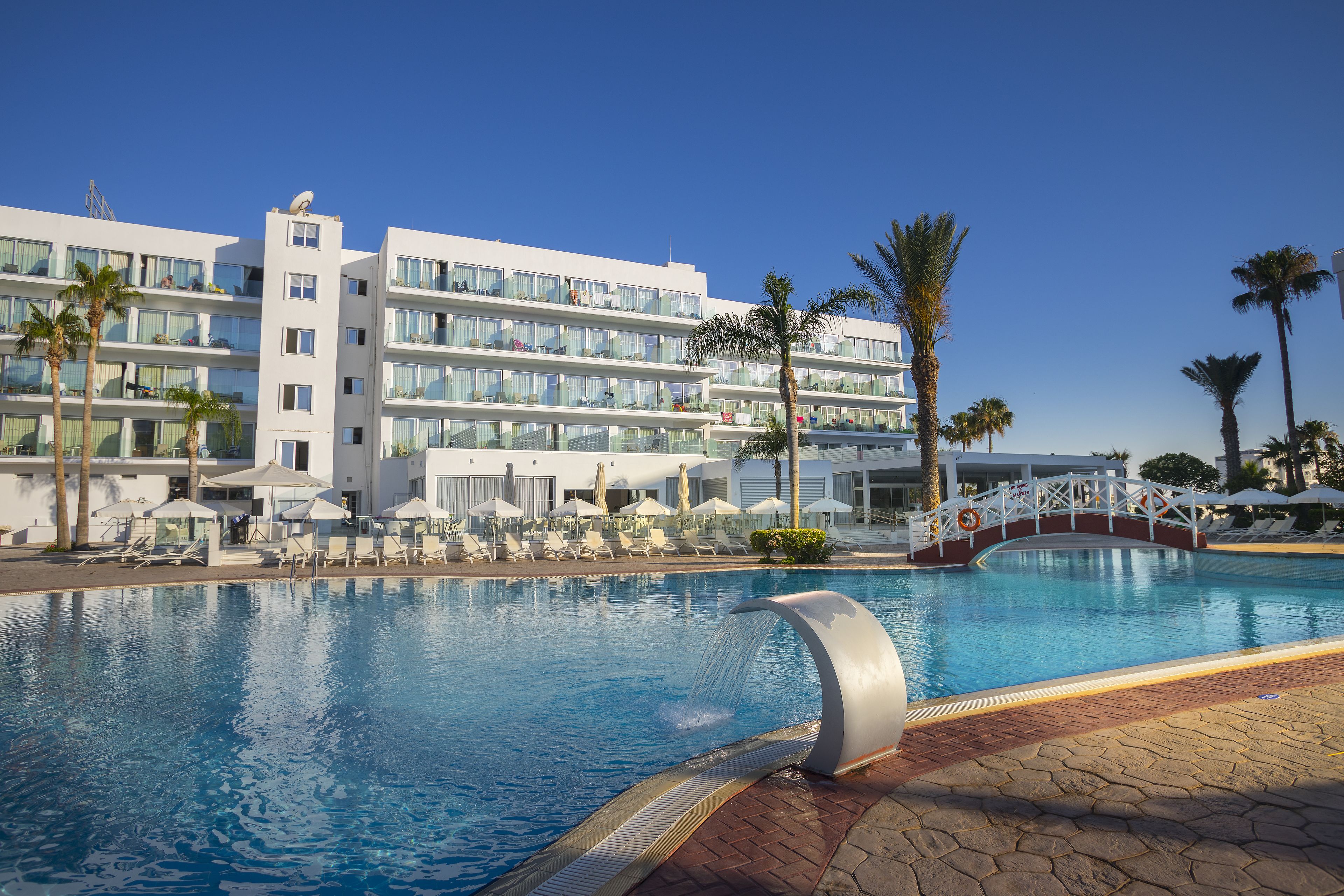 Un hôtel doté d’une piscine, de palmiers et d’un pont.