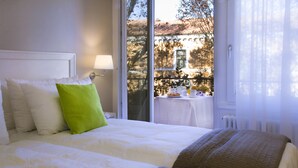 A hotel room with a bed, a window with a view of a building, and a table with a lamp. - Domus Giulio Cesare (Rome)