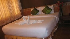 Ein Hotelzimmer mit einem ordentlich bezogenen Bett, einem Bild an der Wand und einer Vase mit Blumen auf dem Nachttisch.