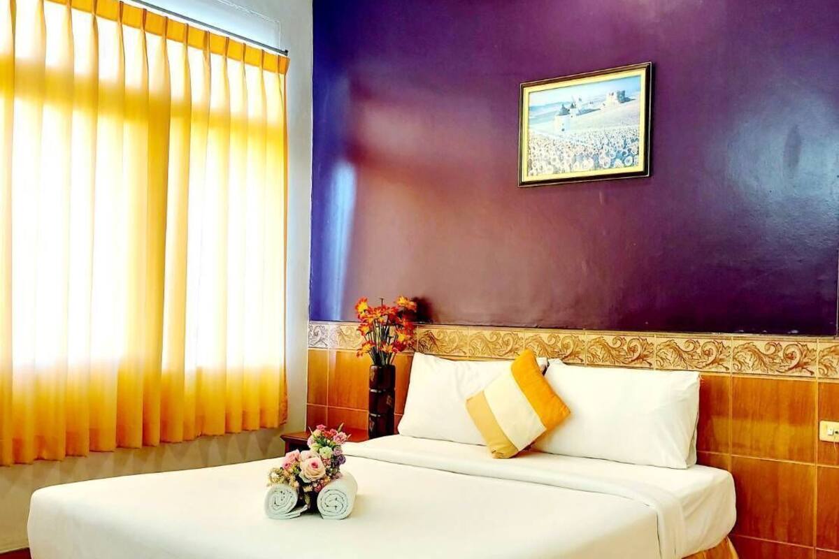 Une chambre d’hôtel avec un lit, des rideaux, un ventilateur de plafond, un tableau accroché au mur et un vase avec des fleurs.