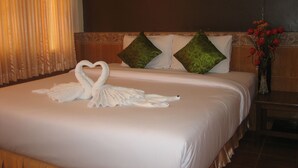 Ein Hotelzimmer mit einem ordentlich bezogenem Bett, einer Herz-Towel-Dekoration, einer Vase mit Blumen und einem Bild an der Wand.