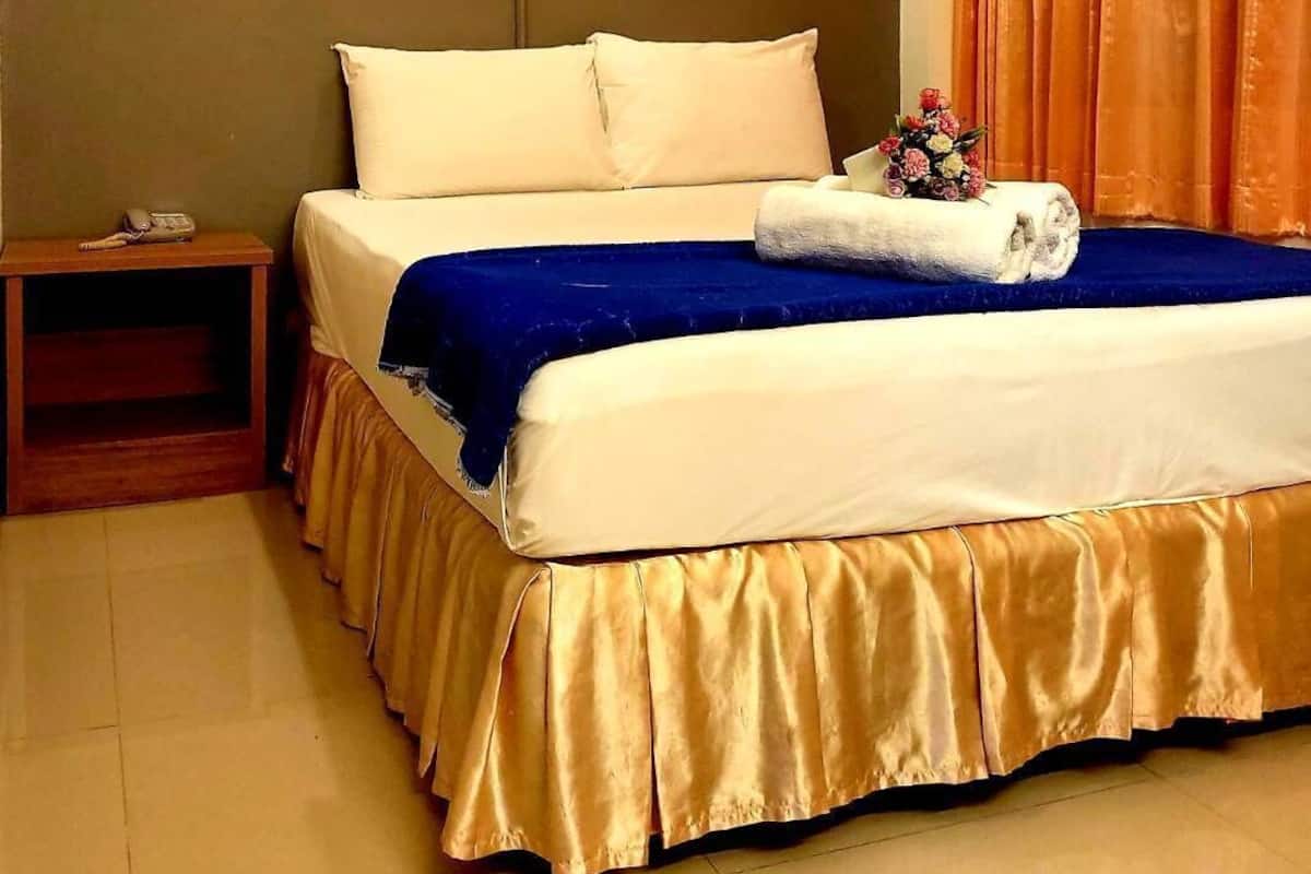 Une chambre d’hôtel avec un lit, une table de chevet, un téléphone et une fenêtre avec des rideaux.