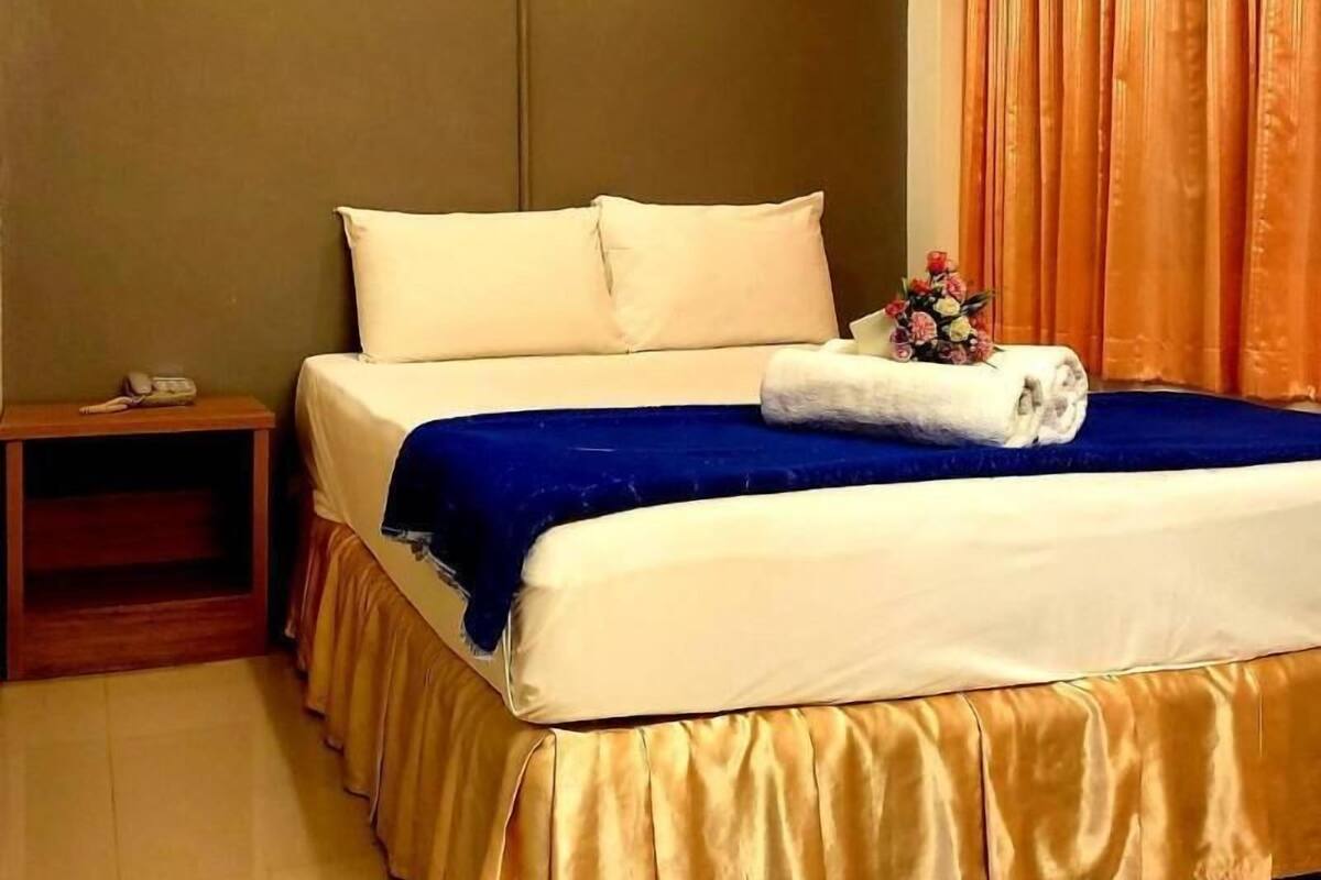 Une chambre d’hôtel avec un lit, une table de chevet, un téléphone et un rideau.
