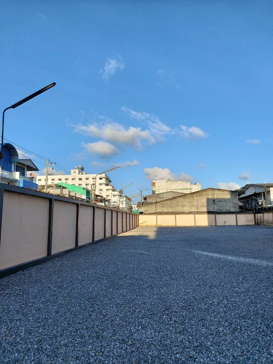 A paved pathway leading to a building with a curved roof, surrounded by a low wall and a streetlight.