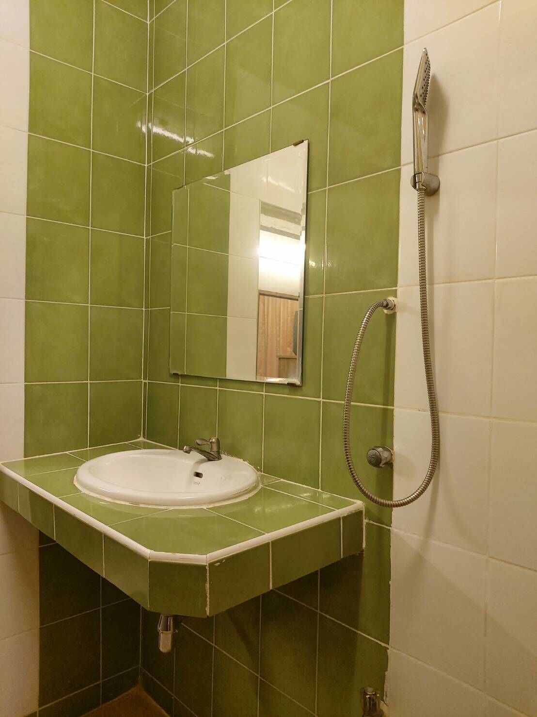 Un baño con azulejos verdes, un lavabo blanco, un espejo y una ducha.