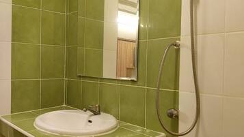 Ein Badezimmer mit grünen Fliesen, einem weißen Waschbecken, einem Spiegel und einer Dusche.