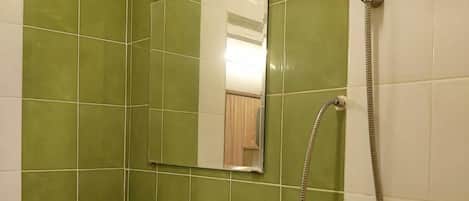 Un baño con azulejos verdes, un lavabo blanco, un espejo y una ducha.